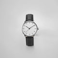 Elegant monochrome luxury watch featuring a clean white dial with thin black hour markers and hands, polished stainless steel case, and supple black textured leather strap displayed against neutral gray background